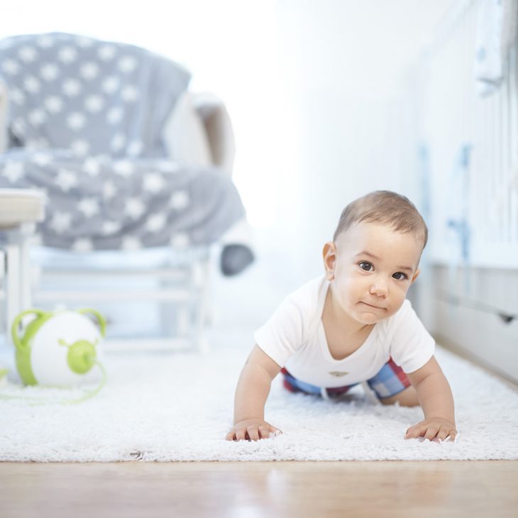 A little boy crawling on a rug, with a green Nosiboo Pro electric nasal aspirator in the background