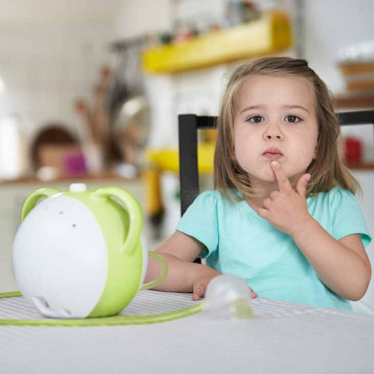 A little girl is thinking about something, with a green Nosiboo Pro electric nasal aspirator in front of her