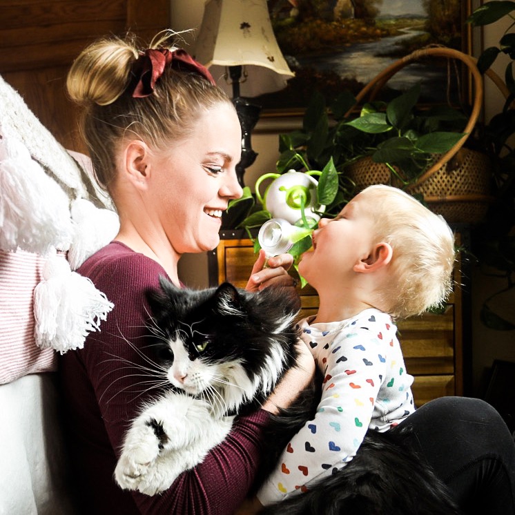 A mother with her child and their cat, using a Nosiboo Pro electric nasal aspirator
