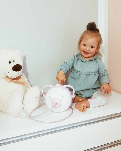 Little girl with Down syndrome sitting on a bed in front of a Nosiboo Pro electric nasal aspirator