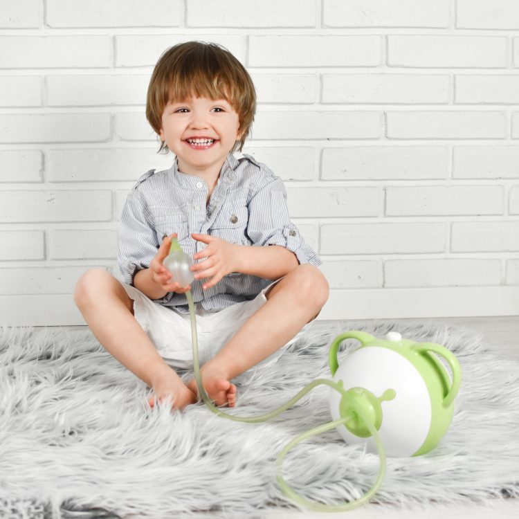 Smiling little boy holding a Nosiboo Pro electric nasal aspirator
